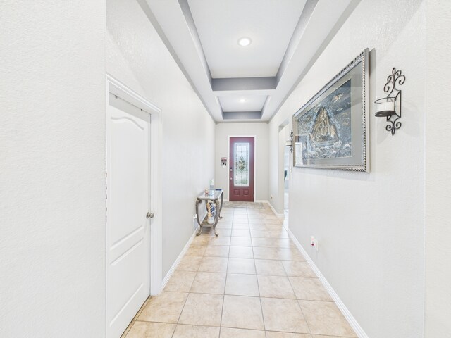 doorway to outside with light tile patterned flooring, a tray ceiling, and baseboards