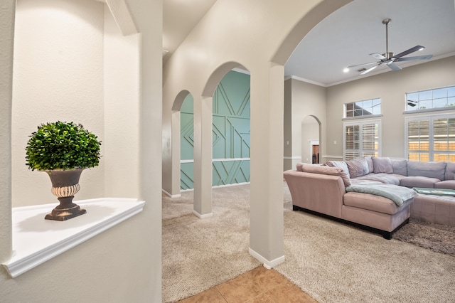 carpeted living room with arched walkways, ceiling fan, tile patterned floors, and baseboards