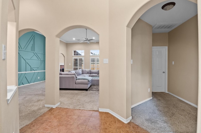 hall with light tile patterned floors, light colored carpet, visible vents, baseboards, and arched walkways