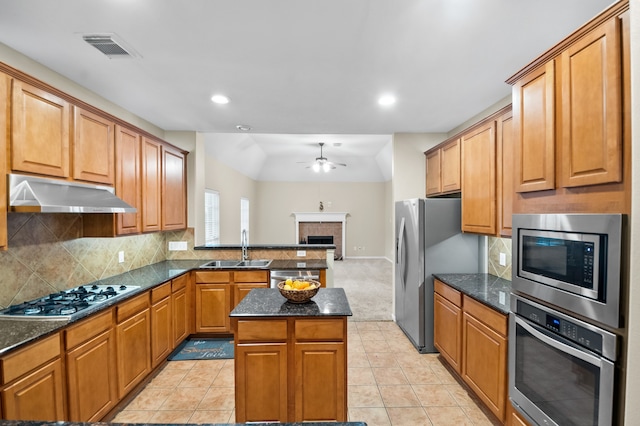 kitchen featuring a sink, a tiled fireplace, stainless steel appliances, under cabinet range hood, and visible vents