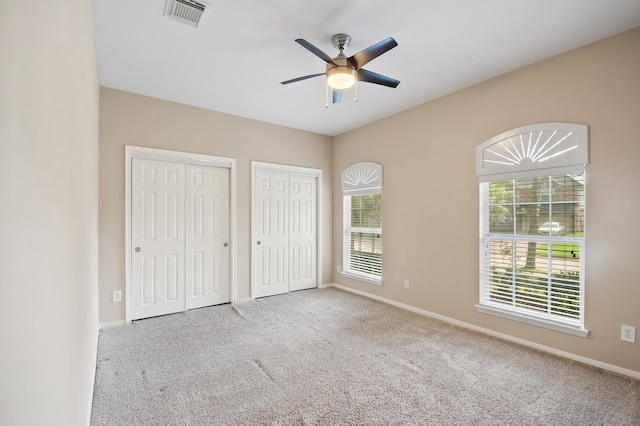 unfurnished bedroom featuring carpet, visible vents, multiple closets, and baseboards