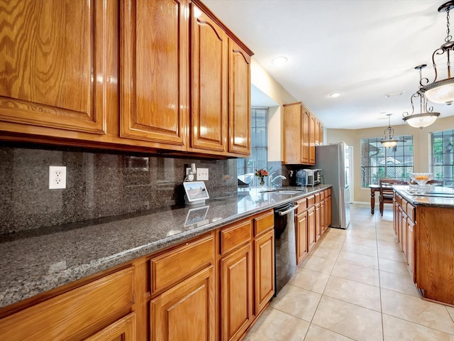 kitchen with light tile patterned floors, dark stone counters, a sink, dishwasher, and brown cabinets