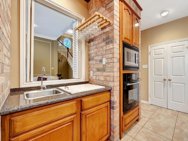 kitchen featuring stainless steel microwave, light tile patterned floors, a sink, black oven, and brown cabinetry
