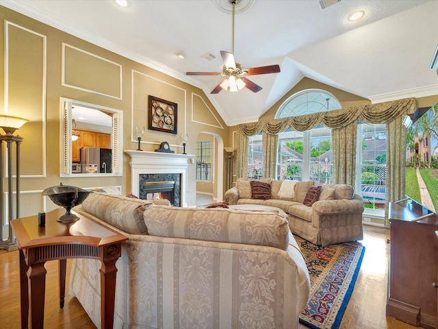 living room with vaulted ceiling, a ceiling fan, wood finished floors, a premium fireplace, and arched walkways