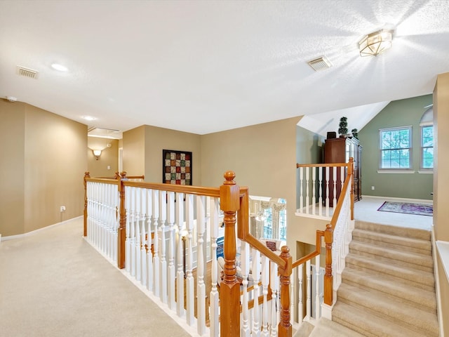 hall with baseboards, visible vents, an upstairs landing, and carpet
