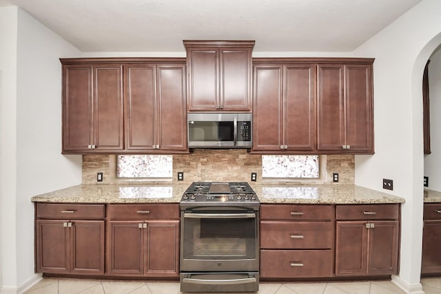 6423 Middlelake Ct, Katy, TX 77450 - kitchen featuring appliances with stainless steel finishes, arched walkways, tasteful backsplash, and light stone counters