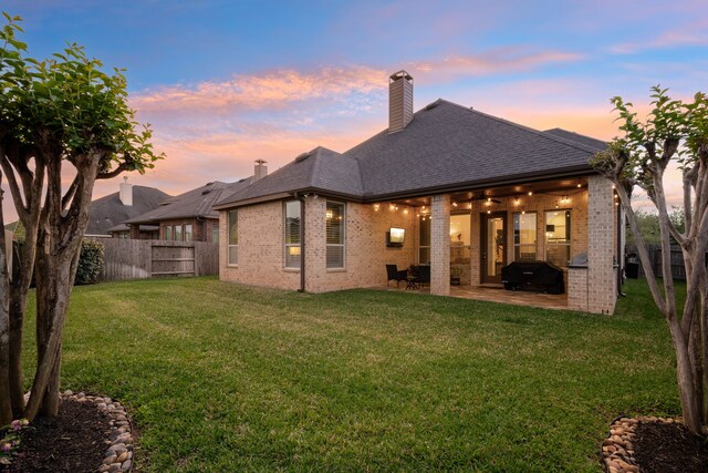 19843 Quarry Stone Ln, Richmond, TX 77407 - back of property at dusk with brick siding, a patio, a chimney, and a shingled roof