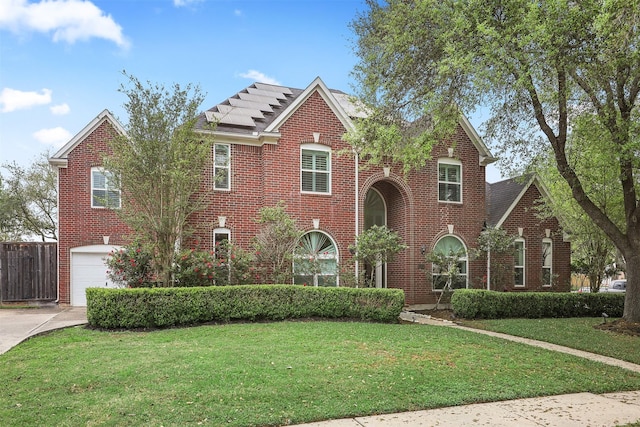 traditional-style house with fence, an attached garage, driveway, a front yard, and brick siding