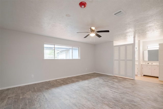 empty room with a textured ceiling, visible vents, baseboards, a ceiling fan, and light wood-type flooring