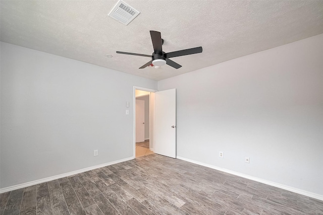 spare room featuring a ceiling fan, wood finished floors, a textured ceiling, baseboards, and visible vents