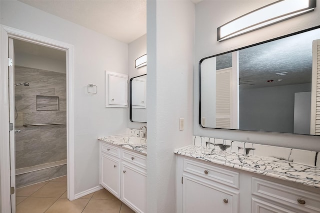 full bathroom with baseboards, tiled shower, two vanities, a sink, and tile patterned flooring