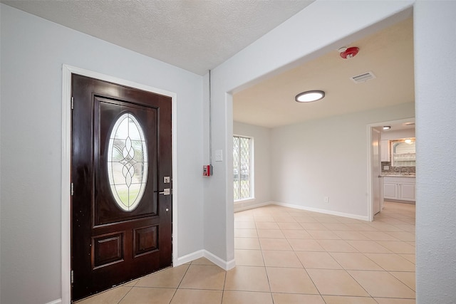 foyer entrance featuring light tile patterned flooring, a textured ceiling, baseboards, and visible vents