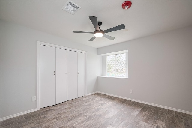 unfurnished bedroom featuring wood finished floors, baseboards, a closet, and visible vents