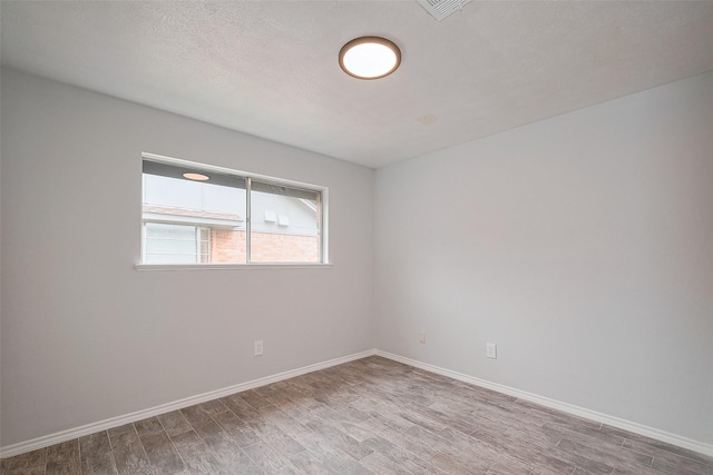 empty room featuring visible vents, a textured ceiling, baseboards, and wood finished floors