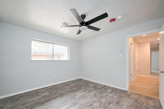 empty room featuring wood finished floors, a textured ceiling, baseboards, visible vents, and ceiling fan