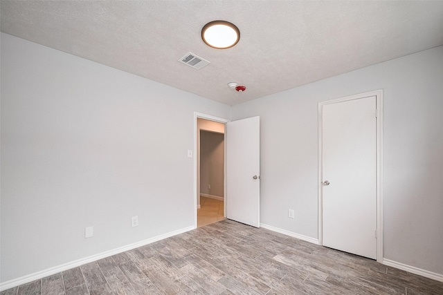 unfurnished bedroom featuring baseboards, a textured ceiling, visible vents, and wood finished floors