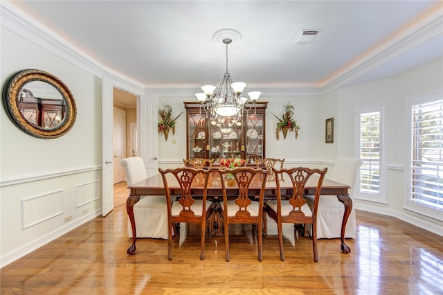 dining room with a chandelier, light wood-style floors, ornamental molding, and a decorative wall
