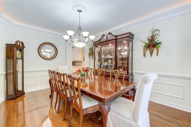 dining space featuring a chandelier, a decorative wall, a wainscoted wall, light wood-style floors, and crown molding