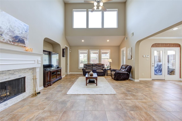 living area with a ceiling fan, healthy amount of natural light, a fireplace, light tile patterned flooring, and a high ceiling