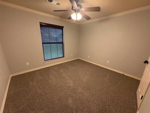 spare room with baseboards, ornamental molding, visible vents, and dark colored carpet