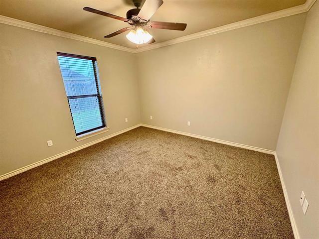 empty room with ornamental molding, baseboards, and dark colored carpet