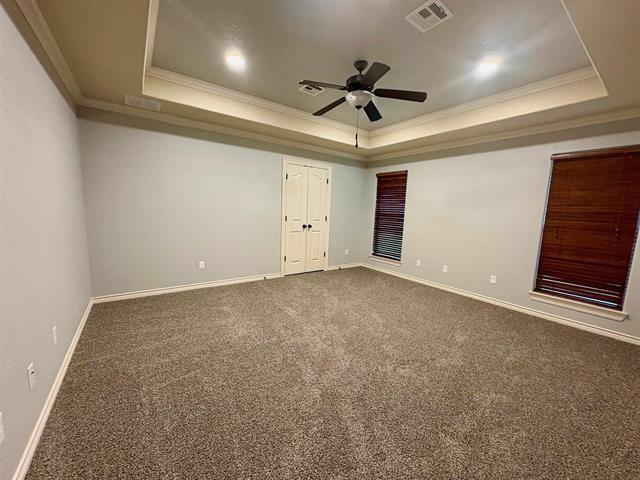 carpeted spare room with a tray ceiling, visible vents, and a ceiling fan