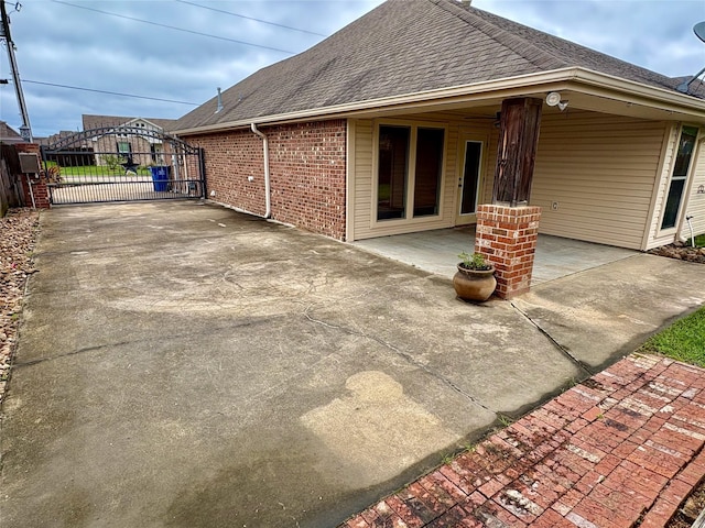 rear view of property featuring a gate, a shingled roof, fence, and a patio
