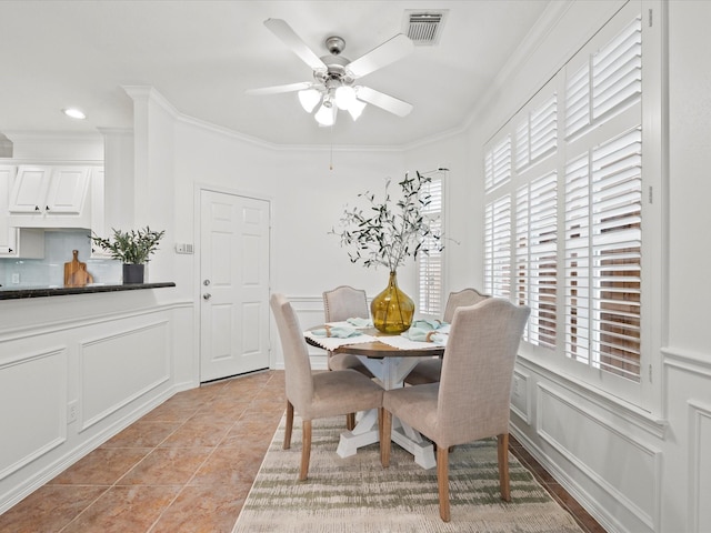 dining space featuring crown molding, a decorative wall, light tile patterned floors, visible vents, and a ceiling fan
