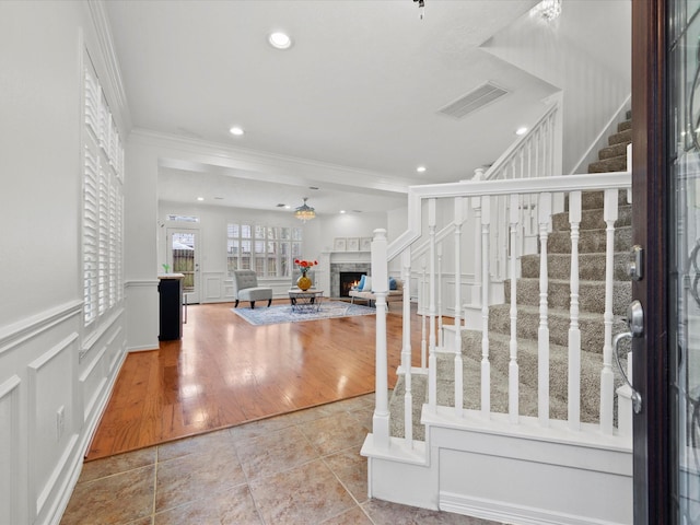 foyer with a warm lit fireplace, a decorative wall, visible vents, crown molding, and stairway