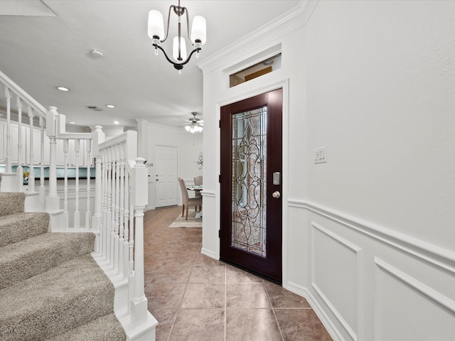foyer featuring crown molding, stairway, light tile patterned floors, a decorative wall, and wainscoting