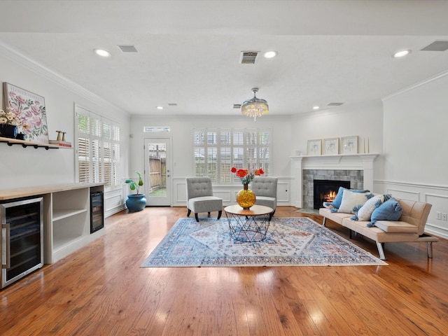 living area featuring visible vents, light wood finished floors, a fireplace, ornamental molding, and wine cooler