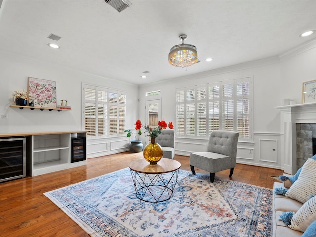 living area with crown molding, wood finished floors, beverage cooler, a decorative wall, and visible vents