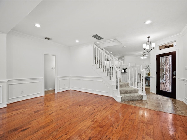 foyer with a notable chandelier, crown molding, stairway, wood finished floors, and visible vents