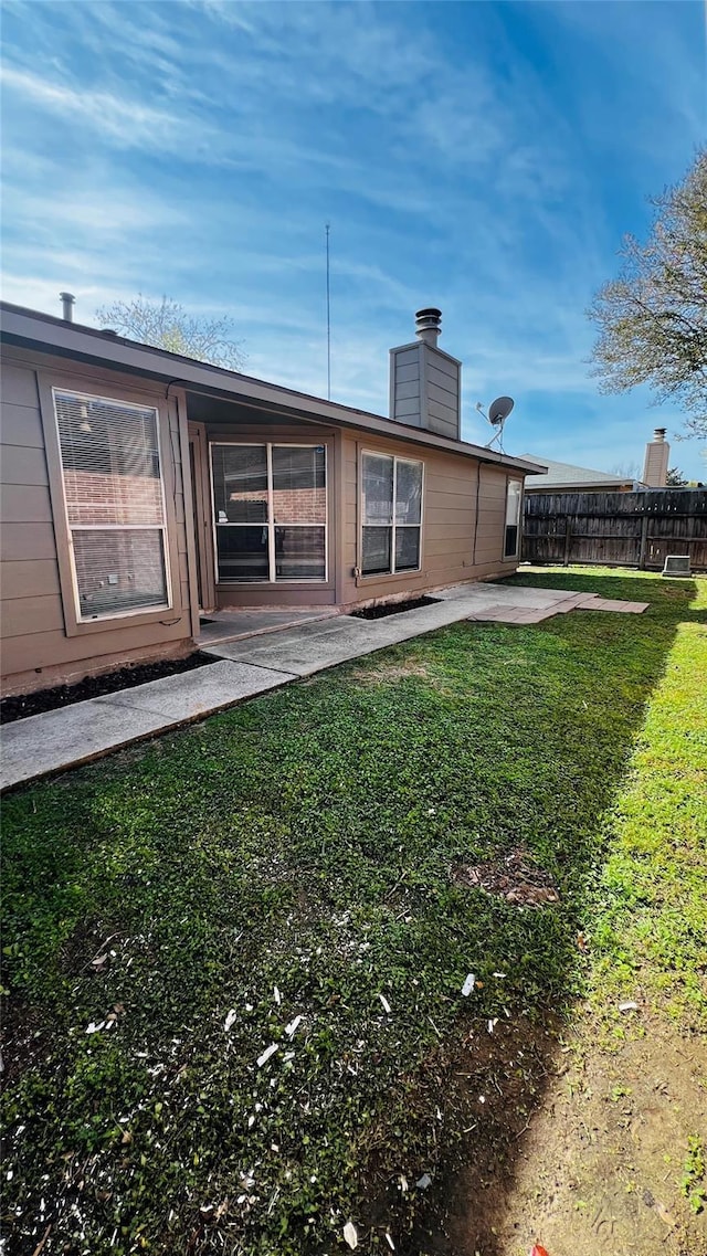 rear view of property with a lawn, fence, a chimney, and a patio