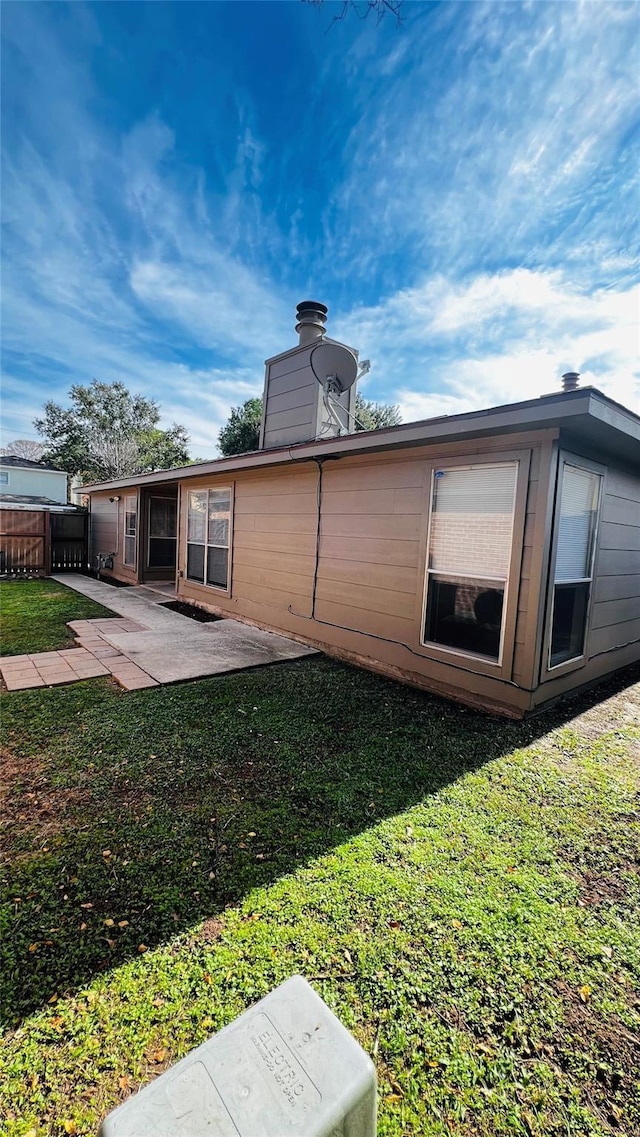 rear view of property featuring fence, a yard, a chimney, and a patio area