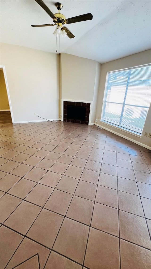 unfurnished living room with baseboards, light tile patterned floors, ceiling fan, and a fireplace