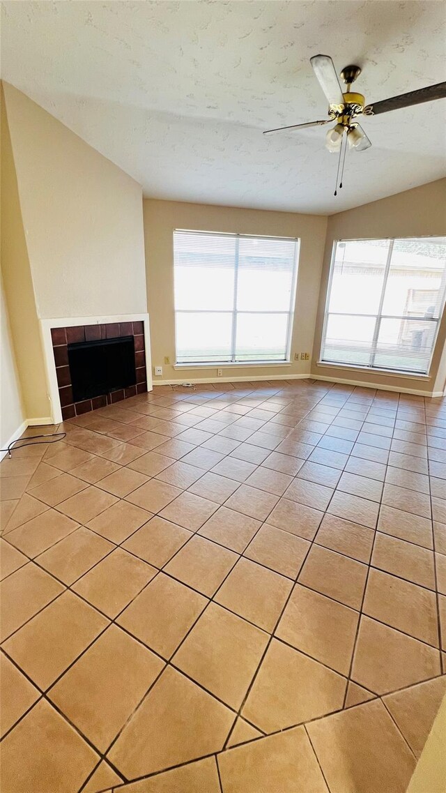 unfurnished living room featuring light tile patterned floors, plenty of natural light, a tile fireplace, and baseboards