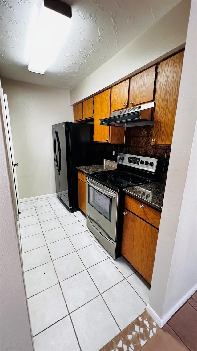 kitchen with brown cabinets, under cabinet range hood, stainless steel electric range oven, backsplash, and dark countertops
