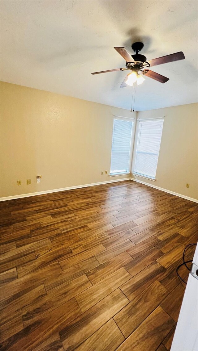 empty room with baseboards, a ceiling fan, and dark wood-style flooring