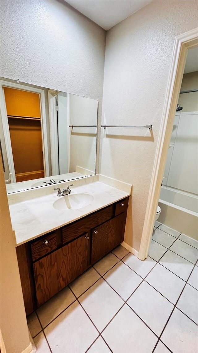 bathroom featuring vanity, toilet, a textured wall, baseboards, and tile patterned flooring
