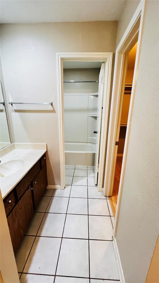 full bath featuring washtub / shower combination, baseboards, tile patterned floors, vanity, and a walk in closet
