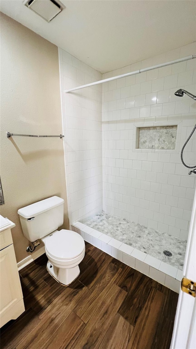 bathroom with wood finished floors, tiled shower, toilet, and vanity