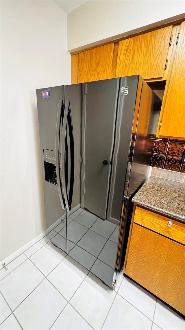 kitchen featuring light tile patterned floors, stone countertops, black refrigerator with ice dispenser, and brown cabinets
