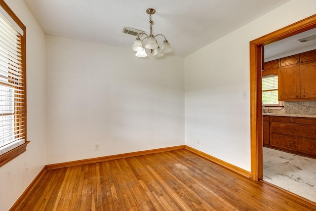 unfurnished dining area with baseboards, a notable chandelier, visible vents, and light wood-type flooring