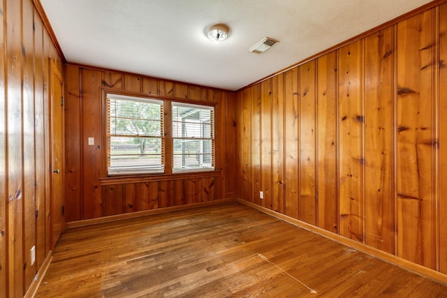 spare room with hardwood / wood-style floors, baseboards, visible vents, and wood walls