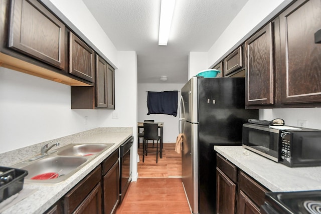 kitchen with dark brown cabinets, appliances with stainless steel finishes, light countertops, a sink, and light wood finished floors