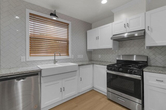 2831 Jones St, Houston, TX 77026 - kitchen featuring stainless steel appliances, extractor fan, decorative backsplash, white cabinetry, and light wood-style flooring