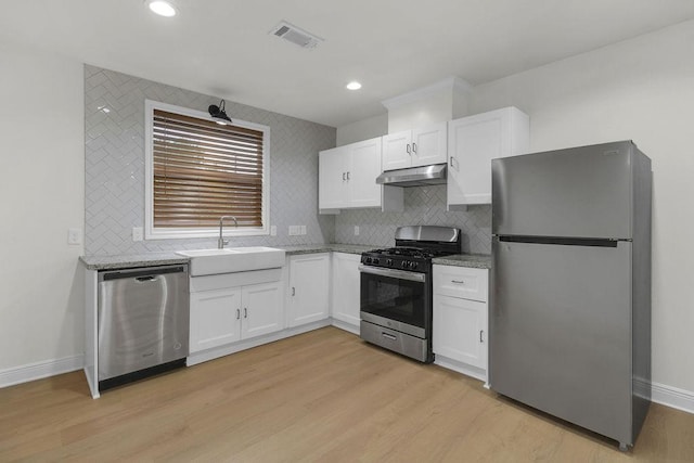 2831 Jones St, Houston, TX 77026 - kitchen with stainless steel appliances, under cabinet range hood, white cabinetry, light wood-type flooring, and recessed lighting