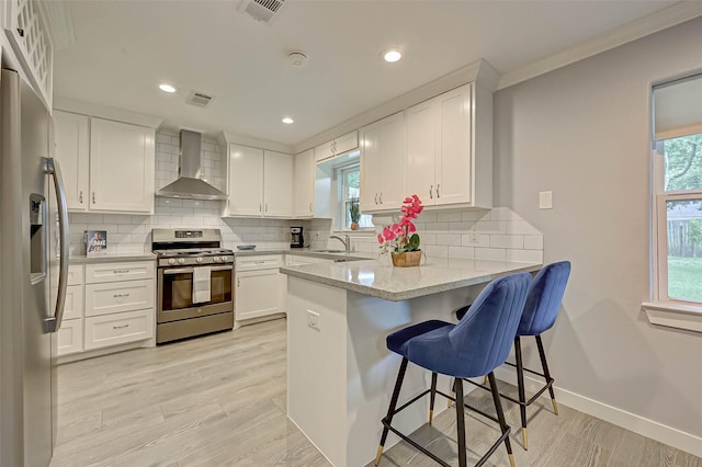 5806 Cartagena St, Houston, TX 77035 - kitchen featuring light wood-type flooring, stainless steel appliances, visible vents, wall chimney range hood, and a peninsula