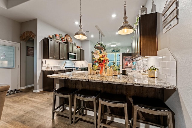9791 Waller St, Conroe, TX 77303 - kitchen with tasteful backsplash, appliances with stainless steel finishes, a peninsula, light wood-style flooring, and light stone counters